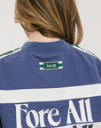 A woman wearing an indigo and green long-sleeved racing shirt with colorblocking and text embroidery.