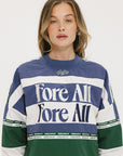 A woman wearing an indigo and green long-sleeved racing shirt with colorblocking and text embroidery.