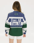 A woman wearing an indigo and green long-sleeved racing shirt with colorblocking and text embroidery.