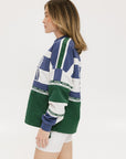 A woman wearing an indigo and green long-sleeved racing shirt with colorblocking and text embroidery.