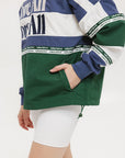 A woman wearing an indigo and green long-sleeved racing shirt with colorblocking and text embroidery.