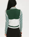 A woman wearing a sleeveless mock-neck sweater with a green and white intarsia knit design and the word 'FORE' written across the front.