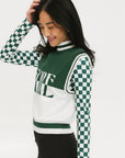 A woman wearing a sleeveless mock-neck sweater with a green and white intarsia knit design and the word 'FORE' written across the front.