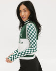 A woman wearing a sleeveless mock-neck sweater with a green and white intarsia knit design and the word 'FORE' written across the front.