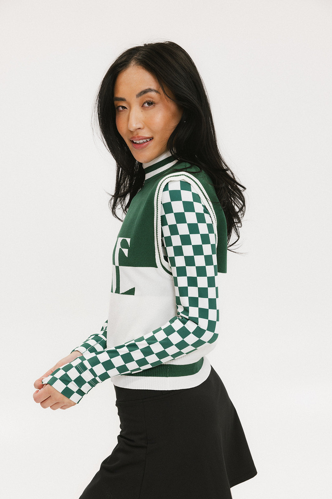 A woman wearing a sleeveless mock-neck sweater with a green and white intarsia knit design and the word 'FORE' written across the front.