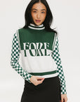 A woman wearing a sleeveless mock-neck sweater with a green and white intarsia knit design and the word 'FORE' written across the front.