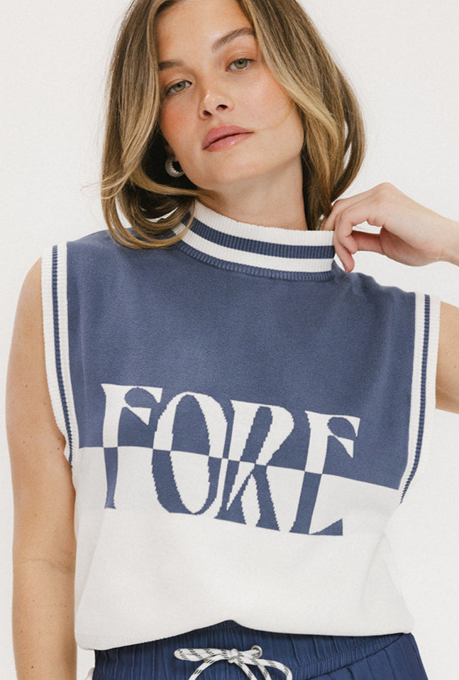 A woman wearing a sleeveless mock-neck sweater with 'FORE' text in blue and white colors.