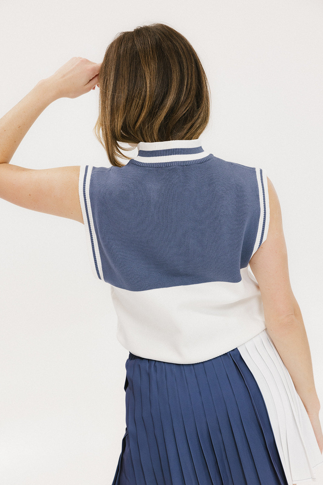 A model wearing an indigo and white intarsia mock neck, sleeveless Fore Sweater.