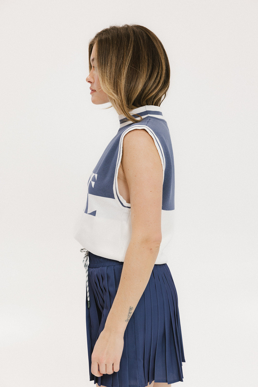 A model wearing an indigo and white intarsia mock neck, sleeveless Fore Sweater.