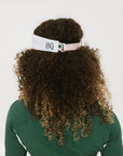 A woman wearing a pink and white 'FORE' visor and a green long-sleeved shirt.