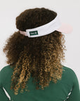 A woman wearing a pink and white 'FORE' visor and a green long-sleeved shirt.