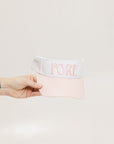 A hand holding a two-toned visor with 'FORE' logo in pink and white colors.