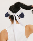 A woman wearing a white and indigo visor with a 'FA' logo on the front and a tied bow on the back.