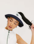 A woman wearing a white and indigo visor with a 'FA' logo on the front and a tied bow on the back.