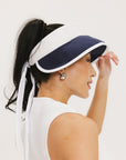 A woman wearing a white and indigo visor with a 'FA' logo on the front and a tied bow on the back.