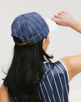 A model wearing a blue and white striped baseball cap with an embroidered logo