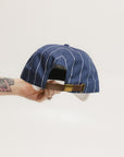A hand holding a blue and white striped baseball cap with an embroidered logo