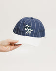 A hand holding a blue and white striped baseball cap with an embroidered logo