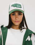 A model wearing a trucker hat with 'Double Bogeys Are Hot' text embroidered on the front, featuring a white mesh back and green visor.