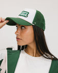 A model wearing a trucker hat with 'Double Bogeys Are Hot' text embroidered on the front, featuring a white mesh back and green visor.