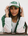 A model wearing a trucker hat with 'Double Bogeys Are Hot' text embroidered on the front, featuring a white mesh back and green visor.
