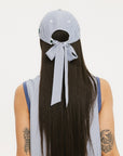 A person wearing a blue and white seersucker baseball cap with the text 'Chasing Balls' embroidered on the front and an oversized bow at the back.