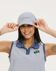 A person wearing a blue and white seersucker baseball cap with the text 'Chasing Balls' embroidered on the front and an oversized bow at the back.