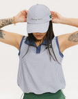 A person wearing a blue and white seersucker baseball cap with the text 'Chasing Balls' embroidered on the front and an oversized bow at the back.