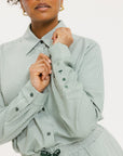 A person wearing a green striped button-up shirt with the sleeves rolled up to the elbows.