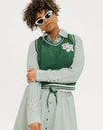A woman wearing a green striped button-up shirt with a collar, sleeve cuffs, and side seam hem, paired with a matching skirt, sunglasses, and green shoes.