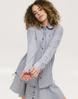 A woman wearing a long, button-up shirt with indigo stripes, featuring a collar, button-down front, and elastic toggles at the side seam hem and sleeve cuffs