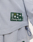 A woman wearing a long, button-up shirt with indigo stripes, featuring a collar, button-down front, and elastic toggles at the side seam hem and sleeve cuffs