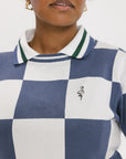 A woman wearing a sleeveless, checkered indigo and white sweater with a mock neck.