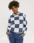 A woman wearing a sleeveless, checkered indigo and white sweater with a mock neck.