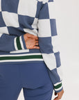 A person wearing a checkered blue and white sweater with green accents and solid blue pants.