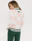 A person is shown from the back wearing a pink and white checkered sweater with a green stripe, paired with green pants.