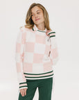 A woman wearing a pink and white checkered intarsia knit sleeveless sweater with a mock neck.