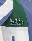 A detail view of a Caitlin Warm-Up Jacket showing a color block design with green, blue, and white panels, and a logo patch on the sleeve.