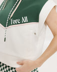 A person wearing a green and white sleeveless hoodie with a hood, matching green and white checkered hat, and green and white checkered skirt. The hoodie has white text and branding on it.