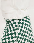 A person wearing a green and white sleeveless hoodie with a hood, matching green and white checkered hat, and green and white checkered skirt. The hoodie has white text and branding on it.