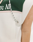 A person wearing a green and white sleeveless hoodie with a hood, matching green and white checkered hat, and green and white checkered skirt. The hoodie has white text and branding on it.