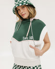 A person wearing a green and white sleeveless hoodie with a hood, matching green and white checkered hat, and green and white checkered skirt. The hoodie has white text and branding on it.