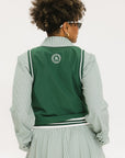 A woman wearing a green sleeveless windbreaker vest with a collar, featuring a white appliquéd logo on the left chest and silicone logos on the upper back.