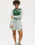A woman wearing a green sleeveless windbreaker vest with a collar, featuring a white appliquéd logo on the left chest and silicone logos on the upper back.