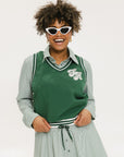 A woman wearing a green sleeveless windbreaker vest with a collar, featuring a white appliquéd logo on the left chest and silicone logos on the upper back.