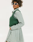 A woman wearing a green sleeveless windbreaker vest with a collar, featuring a white appliquéd logo on the left chest and silicone logos on the upper back.