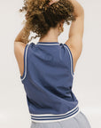 A person wearing a sleeveless blue vest with white stripes and a small logo on the chest area, viewed from the back.