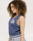 A woman wearing a blue sleeveless windbreaker vest with a bold logo on the chest, ribbed armholes, and silicone logos on the upper back.