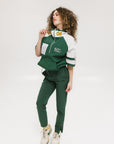 A woman wearing a green and white hoodie with a half-zip design, kangaroo pocket, and decorative woven ribbons.
