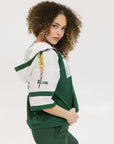 A woman wearing a green and white hoodie with a half-zip design, kangaroo pocket, and decorative woven ribbons.